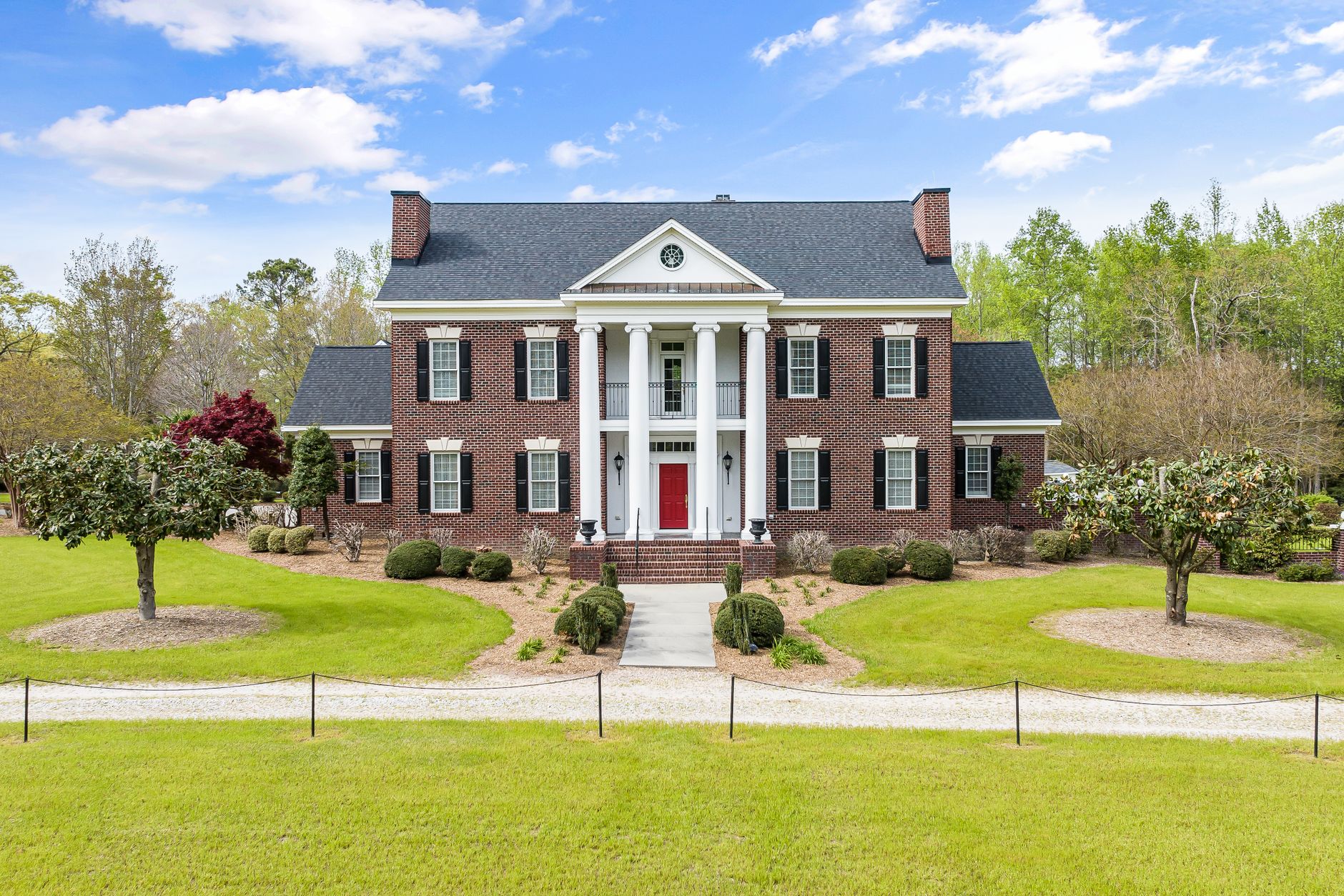 symmetrical image of a residential building with columns and a garden with green lawn
